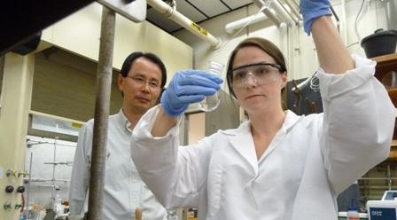 woman conducting an experiment in a lab under the watchful eye of a faculty member