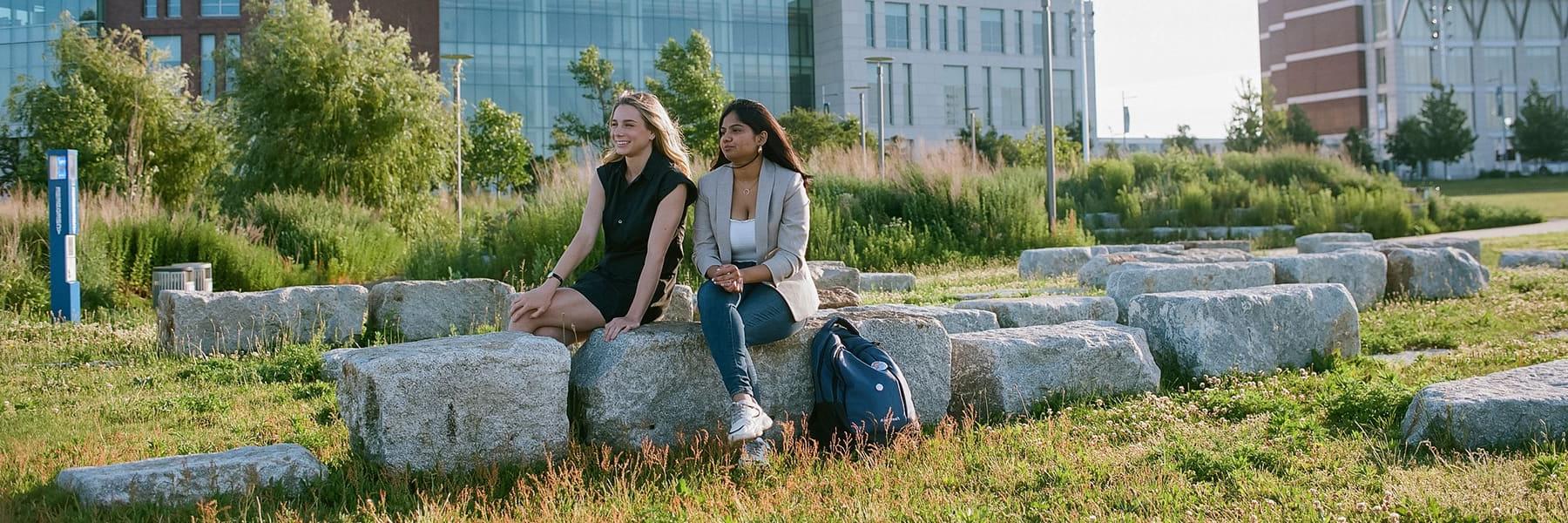 Two students sit on rock benches on campus center lawn.