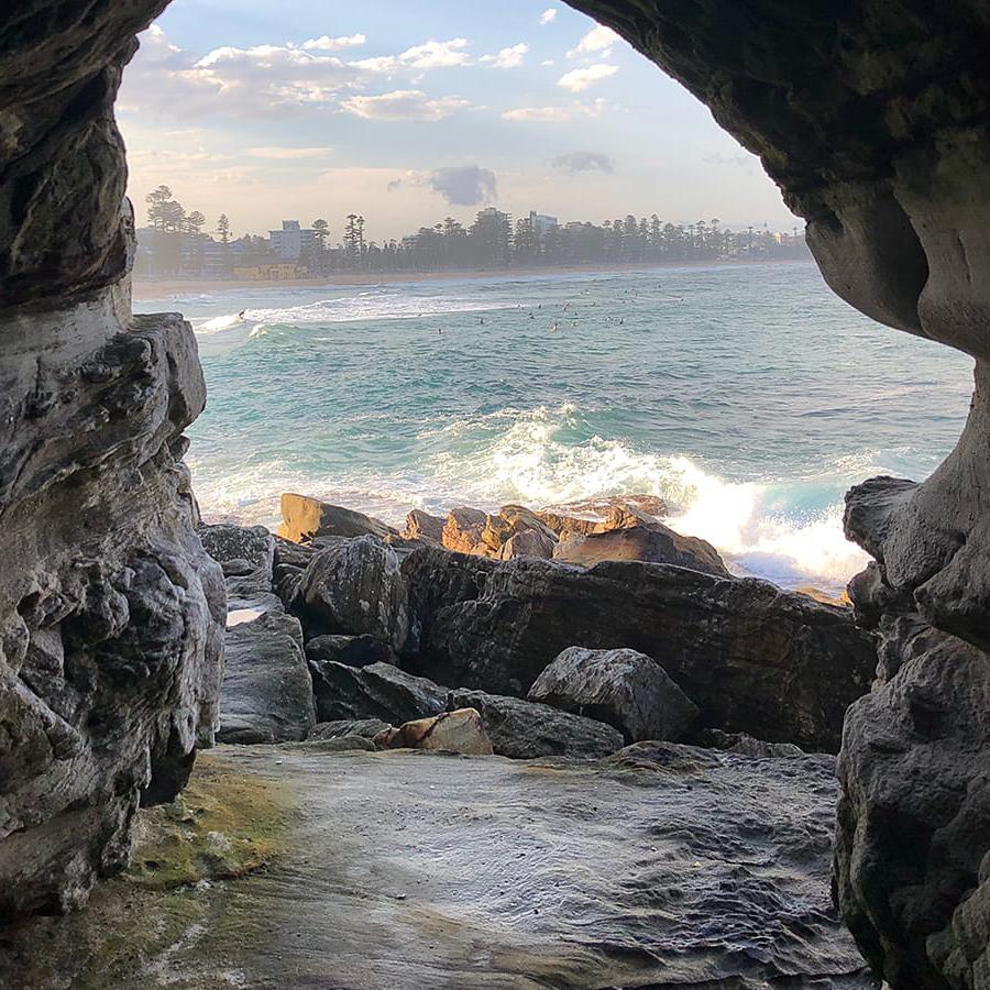 View of Manly Beach through a rock arch with city showing in background in Sydney Australia.