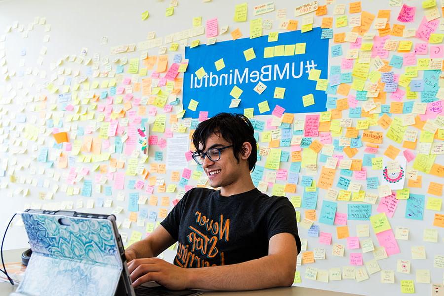 Student at campus center table with giant wall of stickies and prompt that states be mindful behind him.